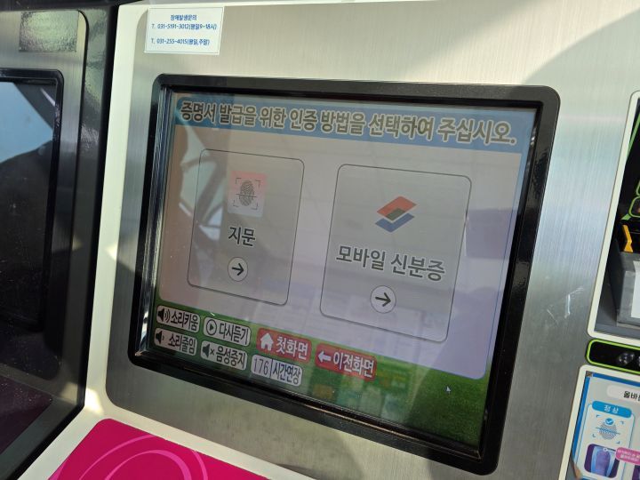 무인민원발급기 앞에서 스마트폰으로 모바일신분증을 인증하려는 사람의 모습(기기 화면과 스마트폰이 동시에 보이는 장면)