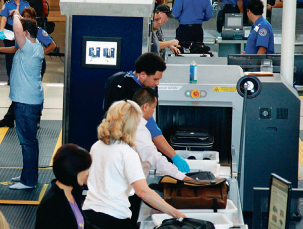 공항 보안검색대 앞에서 바구니에 노트북과 외투를 올려놓는 장면